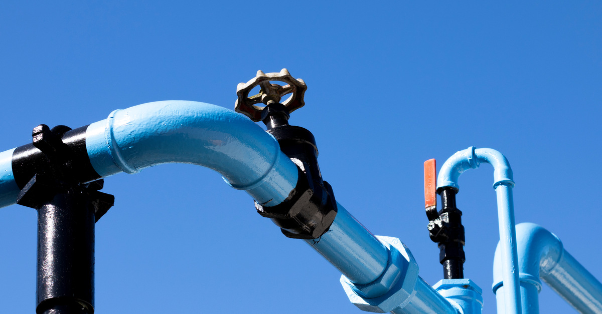 A line of blue pipework on top of a pole with black knobs and red levers attached to it beneath a blue sky.