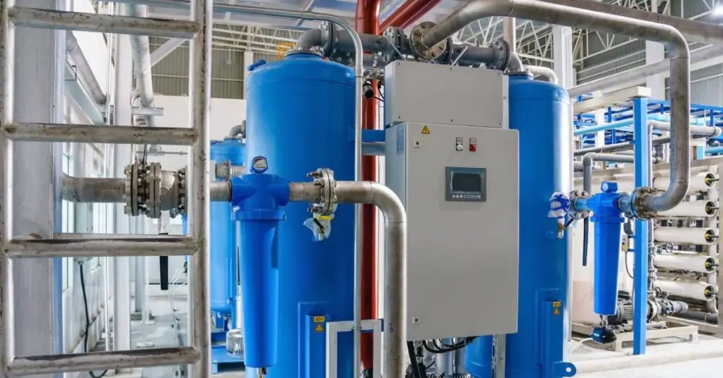 A blue air compressor, up close, with pipes attached to it in front of a ladder leading up to scaffolding.