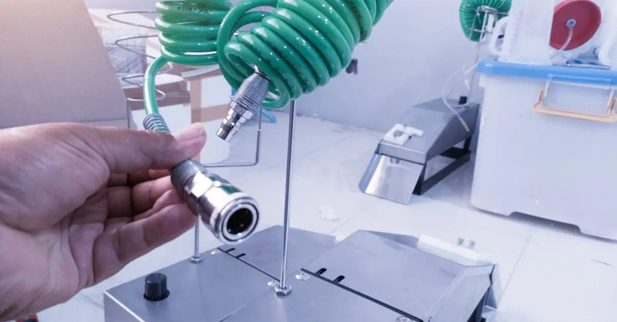 A person’s hand holding the nozzle of a green curled-up hose over a shiny metal machine getting ready to use it.