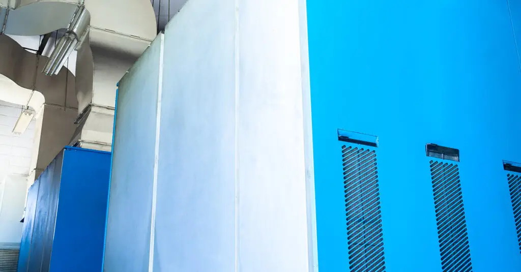 A close-up of two large air compressor systems inside of a factory attached to ducts going into the ceiling.