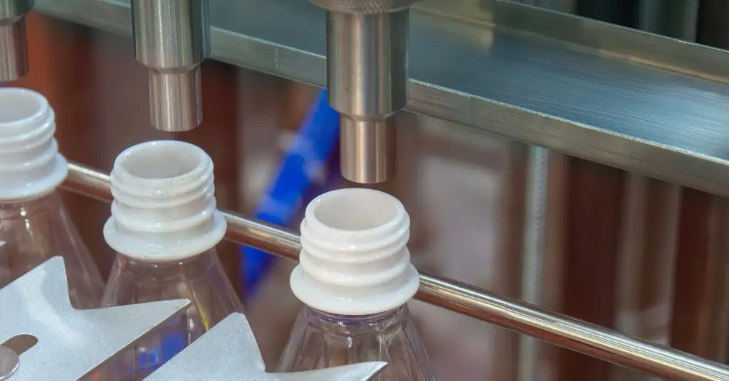 Three bottles with white tops, up close, about to be filled in a food and drink processing facility. - US Air Compressor Three bottles with white tops, up close, about to be filled in a food and drink processing facility.