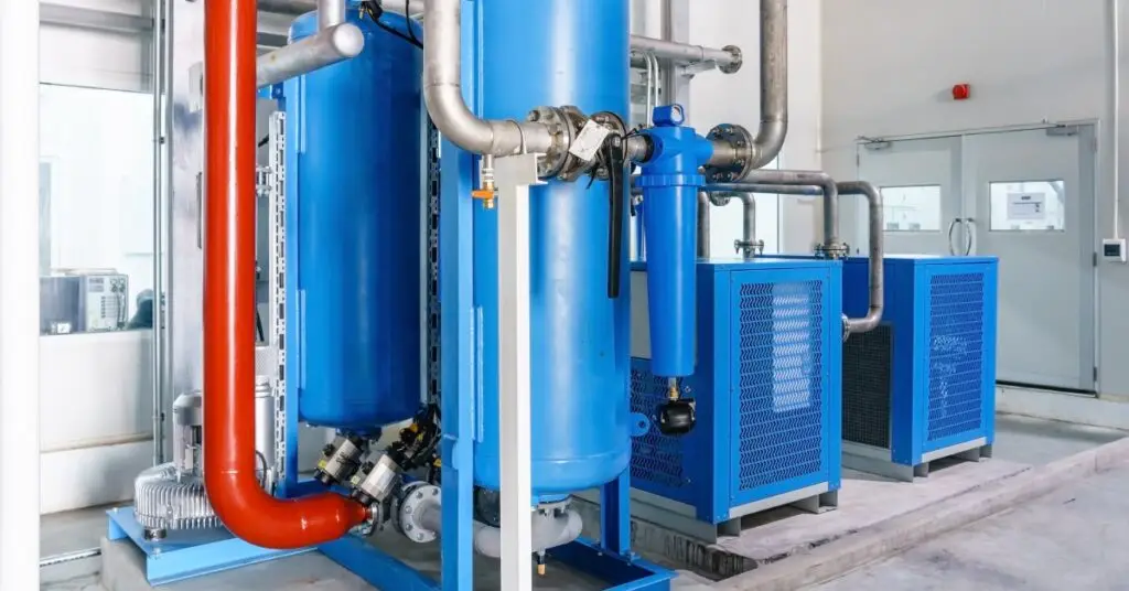 A blue air compressor system attached to silver metal pipes in a warehouse with concrete floors.