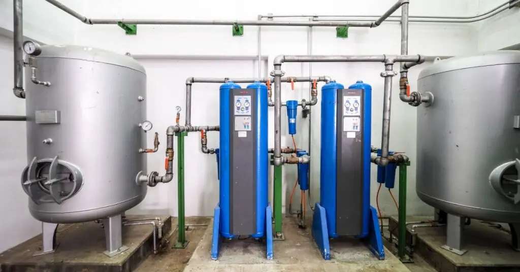 An industrial air compressor system with two large blue air compressors and a silver machine on either side.