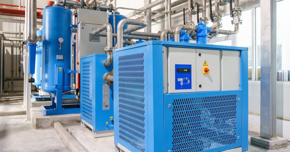 An industrial air compressor system with bright blue machinery and silver pipes set up in a warehouse.