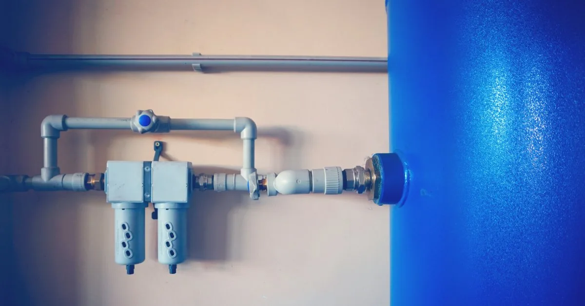 Guide de dimensionnement du système de tuyauterie de votre compresseur d'air - US Air Compressor A gray control air valve is attached to a plain, beige wall and connected to a blue air compressor.