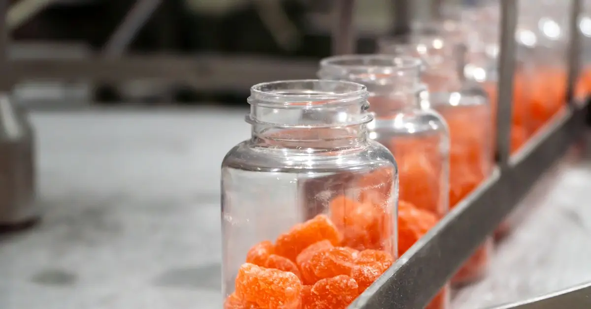 Pourquoi choisir des compresseurs à vitesse fixe plutôt qu'un variateur de fréquence ? - Compresseur d'air américain A manufacturing conveyor belt moving several plastic jars full of orange gummy vitamins in a row.