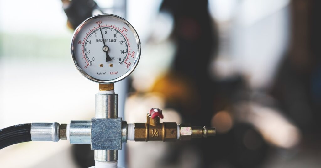 A close-up of a pressure gauge attached to a compressed air system. The gauge shows a reading of 100.