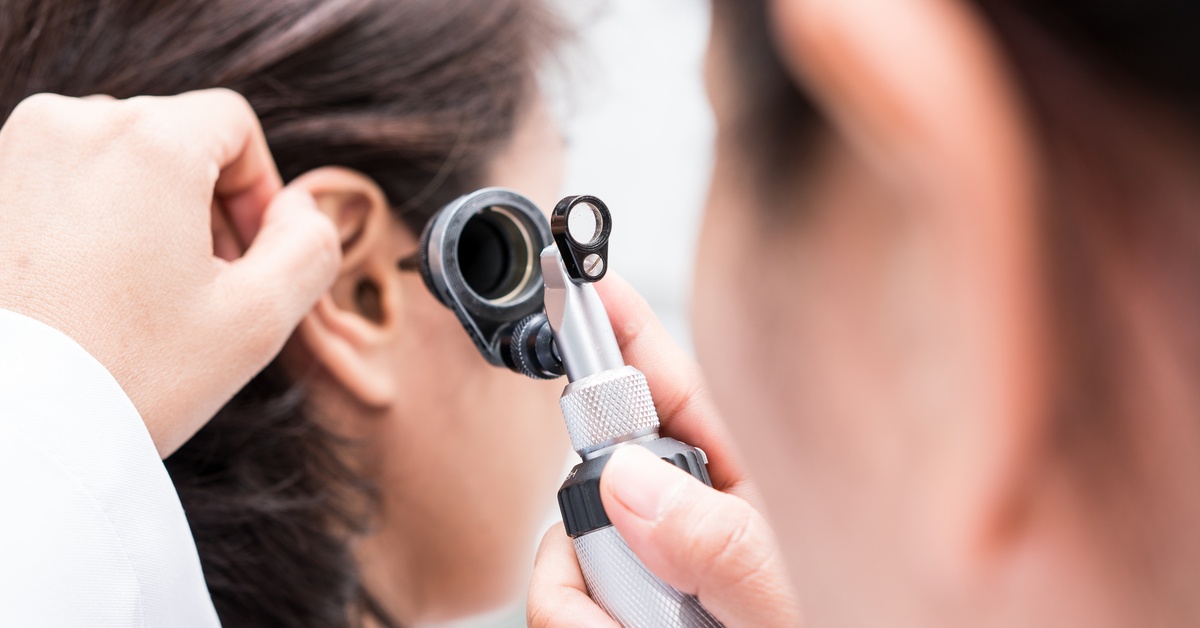 A doctor uses an otoscope to look in a patient’s ear. The doctor is out of focus in the foreground of the image.