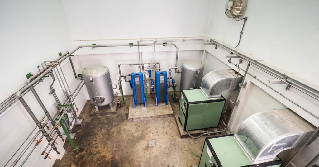 An aerial view of a room in a power plant with silver, blue, and green air compressor and dryer machines.