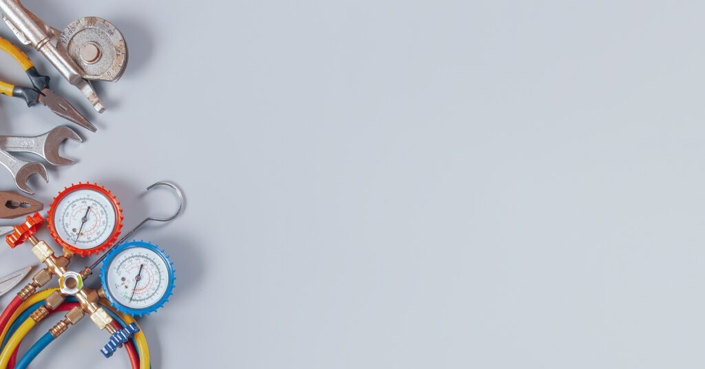 A collection of HVAC and air compressor maintenance tools, such as pliers, wrenches, and an air gauge on a gray background.