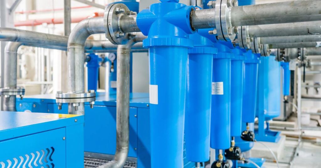 usaircompressor-387272-air-dryer-filter-blogbanner1 - US Air Compressor A line of refrigerated air dryer ultrafilters attached to industrial air compressors in a brightly lit room.