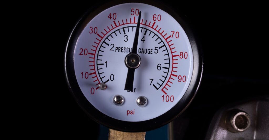 A close-up of an air pressure gauge with black and red numbering on a white background in a dark room.