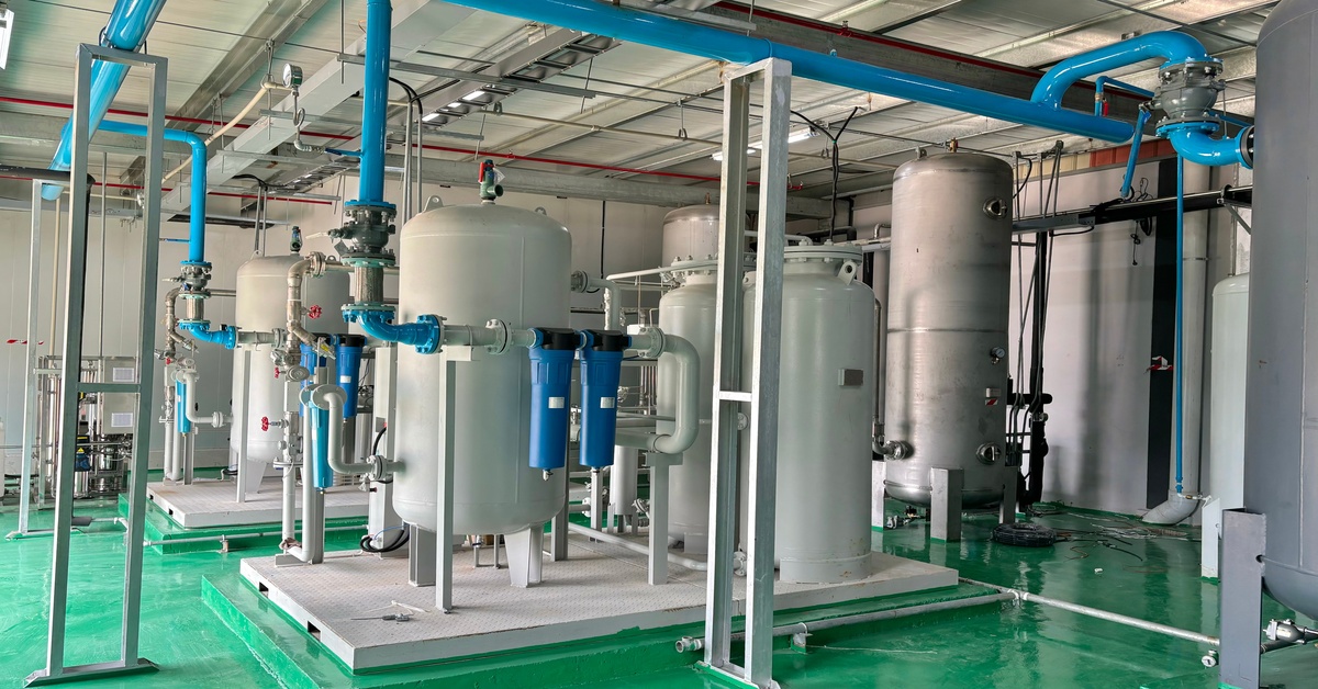 Two gray air compressor systems with blue pumps and pipes in an industrial space with green flooring.