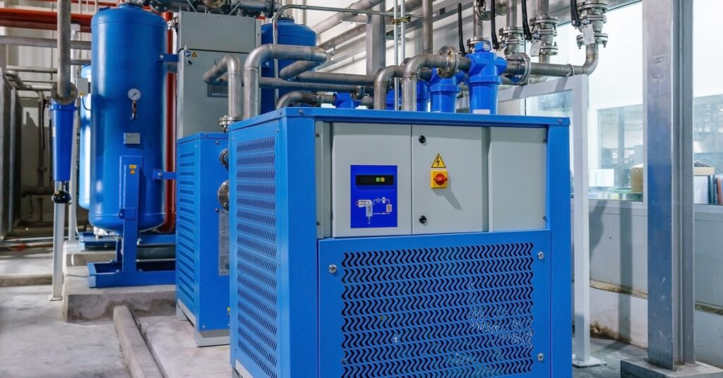 A blue air compressor system with silver and red pipes sitting near the wall of an industrial building.