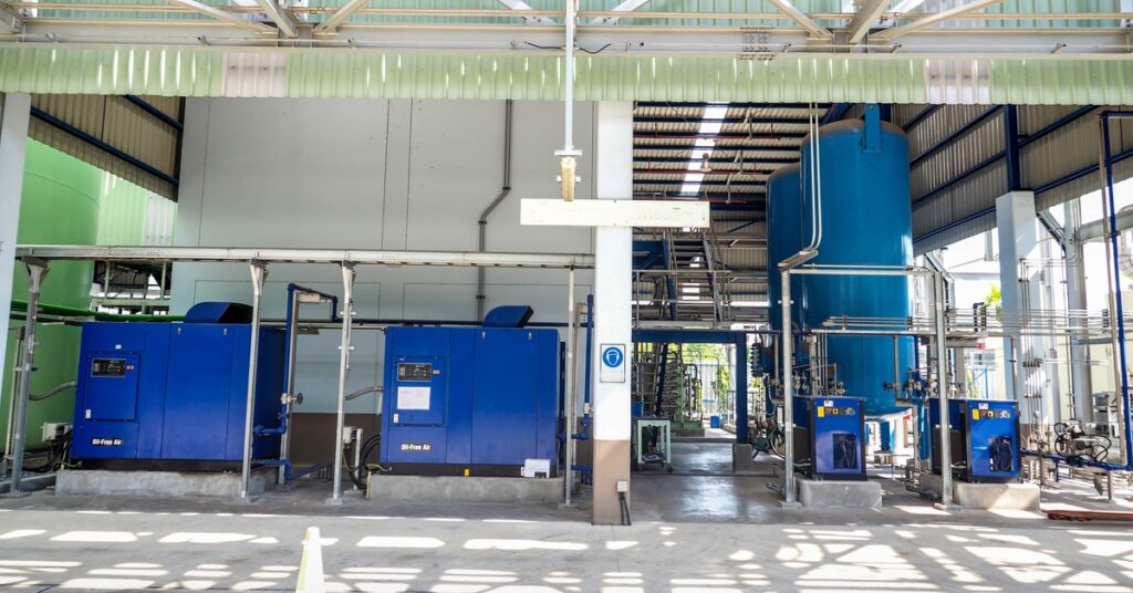 An array of pipes and air compressors in an outdoor industrial environment. The compressors are painted blue.